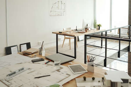 Two workplaces consisting on tables with sketches, blueprints, gadgets, samples and other supplies in large contemporary openspace officeの写真素材