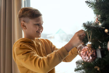 Happy boy in anticipation of New Year standing at Christmas tree and hanging toy on twigの写真素材