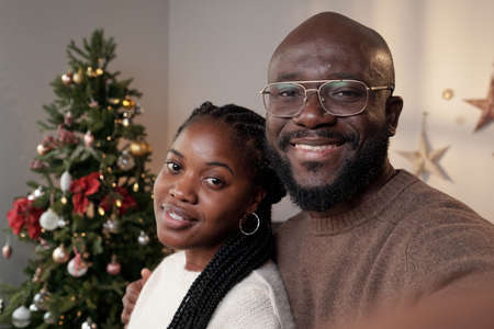 Happy young affectionate couple in casualwear standing against decorated xmas tree in home environmentの写真素材