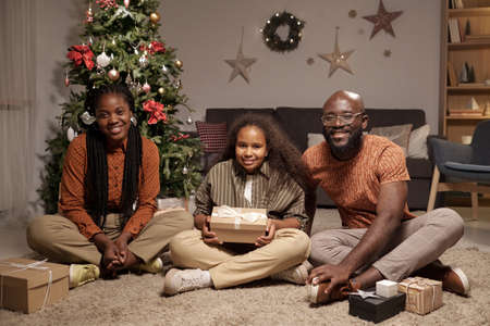 Contemporary young family of parents and cute daughter sitting on the floor in living-room against decorated xmas treeの写真素材
