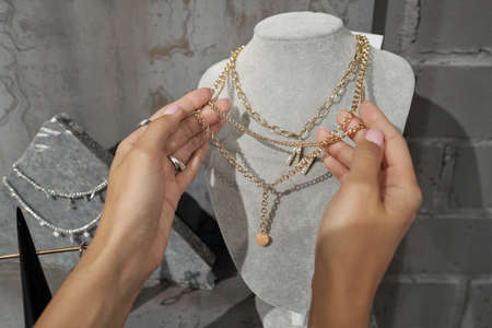 Hands of young female consumer holding gold necklace on mannequin while choosing jewelry in luxurious boutiqueの写真素材