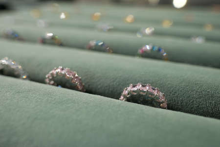 Beautiful ring with gemstones among rows of other luxury jewelry between grey velvet holders on large displayの写真素材
