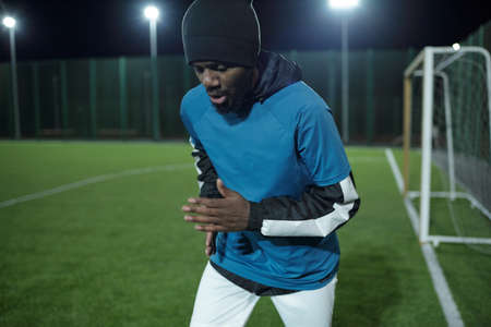 Bearded African soccer player in professionall sports uniform running along football field during...