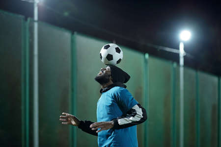 Young professional soccer player with ball on his forehead practicing difficult exercise before match or gameの写真素材
