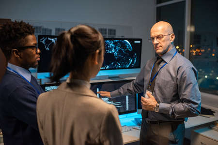 Bald mature director of software company giving instructions to young intercultural subordinates...