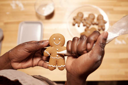 Hands of young African female applying white glaze on gingerbread cookie while making festive food for guests before holidayの写真素材