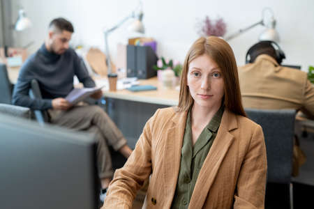 Young elegant businesswoman sitting in front of computer monitor against two male co-workers