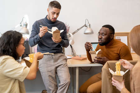 Four young intercultural office workers having chinese wok for lunch by workplaceの写真素材