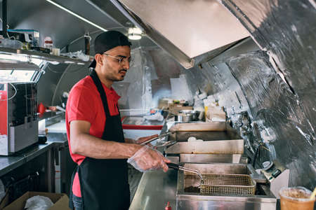 Young clerk of food truck frying snacks in large amount of oil or fat in street truck