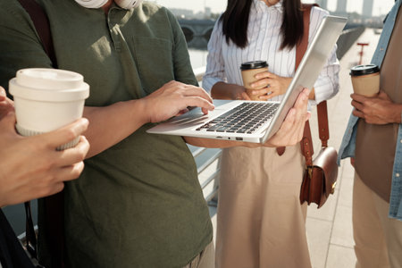 One of four colleagues holding laptop during network at outdoor meeting