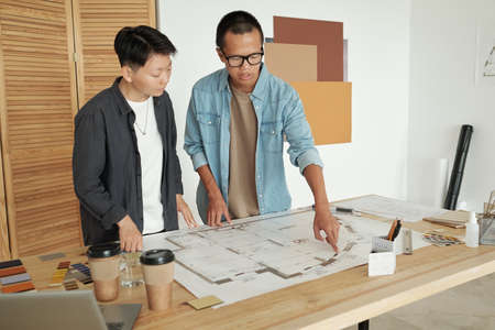 Two young Chinese engineers in casualwear discussing sketch on blueprintの写真素材