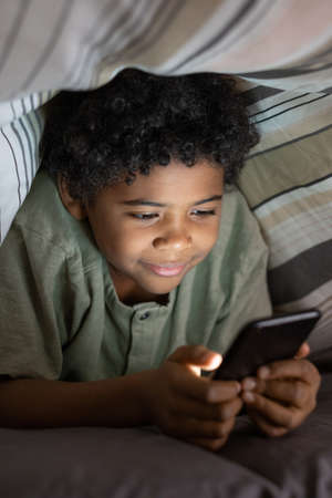 Content African American boy with curly hair addicted to gadget watching video on smartphone under...