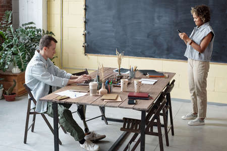 Young intercultural businessman with laptop and businesswoman with smartphone co-working in modern officeの写真素材