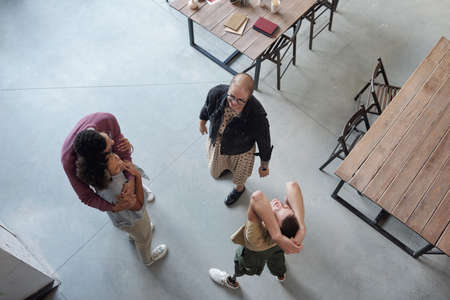 Overview of happy co-workers enjoying break while two of them embracing, man with leg prosthesis...