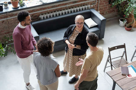 Team of young intercultural people standing in contemporary office and having discussion of working...