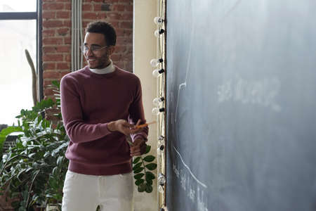 Young successful economist in casualwear explaining financial data or graph to colleagues while pointing at blackboardの写真素材