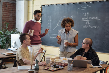 Group of young contemporary colleagues having pizza and drinks during discussion of working points at lunch breakの写真素材