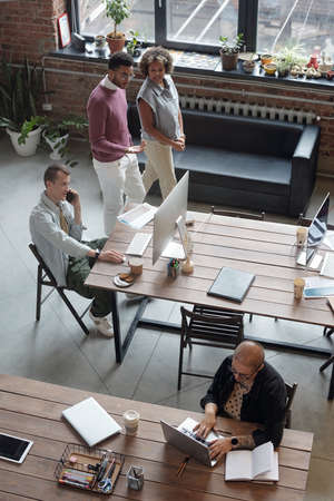 Two young colleagues passing by their co-workers while moving along office and discussing working pointsの写真素材