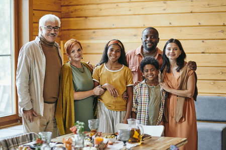 Happy interracial family of three generations standing by served festive table and looking at you with smilesの写真素材