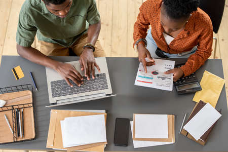 Above view of blackwoman analyzing bill with boyfriend while he filling online tax form on laptop