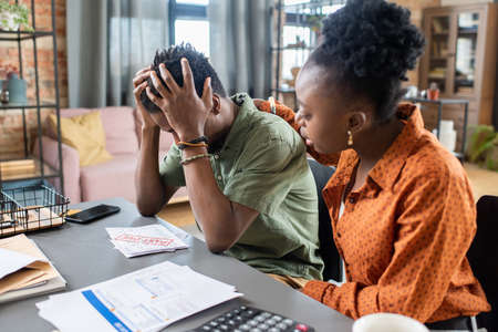 Disappointed blackman holding head in hands while being confused with overdue payment, his...