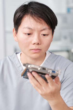 Serious female technician looking at hardware in her hand while repairing it in workshopの写真素材