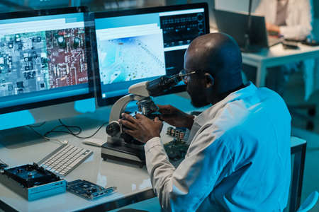 Contemporary young African scientist with microscope working in front of computer monitorsの写真素材