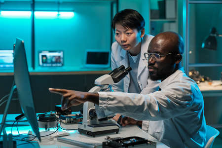 Confident African scientist pointing at computer screen while explaining something to female colleagueの写真素材