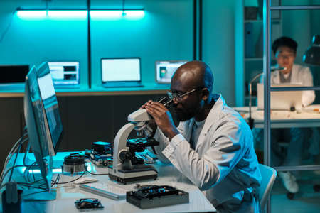 Young African laboratory worker looking in microscope during scientific investigationの写真素材