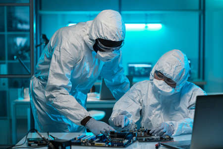 Two contemporary lab workers in protective coveralls consulting about repairment of motherboard or microprocessorの写真素材