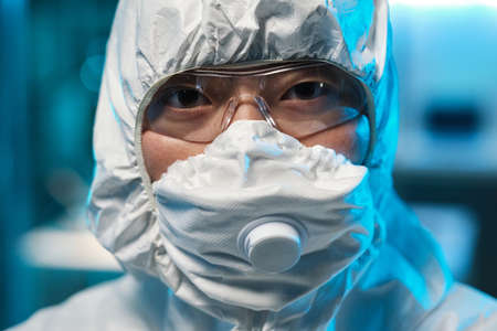 Face of young Asian female scientist in protective respirator, eyeglasses and coverallsの写真素材
