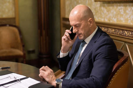 Mature businessman in elegant suit arranging appointment with someone whom he is talking on mobile phoneの写真素材