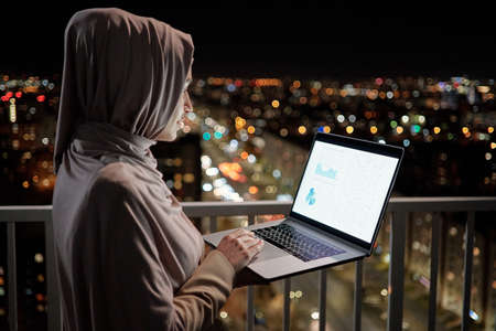 Young female economist analyzing financial graph on laptop screen while working late at nightの写真素材