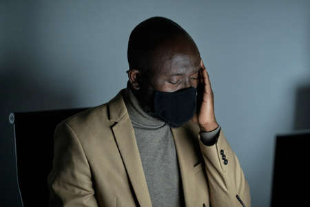 Tired African businessman with headache touching head while working late in the officeの写真素材