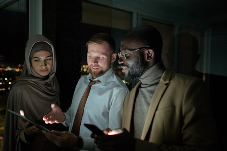 Successful broker explaining online financial information to his intercultural colleagues at night meeting in officeの写真素材