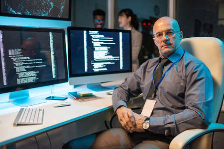 Confident mature male manager of it-engineering company sitting in armchair by workplace and looking...