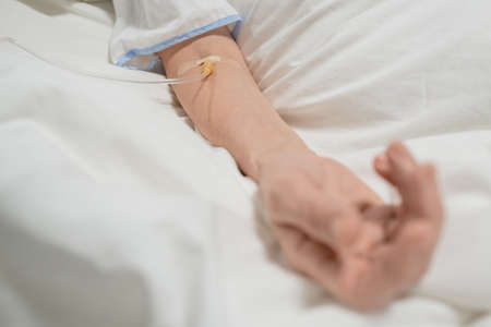 Close-up of senior woman lying in bed with drip in her arm, she is under the anesthesia