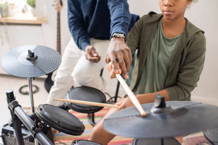 African male teacher explaining biracial schoolgirl with drumsticks how to play drumkit at home lessonの写真素材