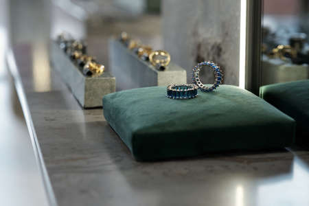 Part of display with two rings on top of square velvet cushion against two rows of other jewelry itemsの写真素材