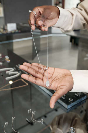 Hands of young African woman showing silver chain with pendant to buyer while holding it over...