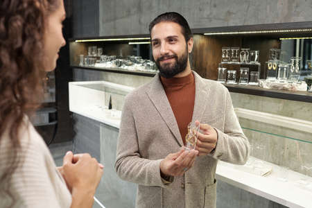 Happy young man and his girlfriend choosing new earrings while visiting large jewelry boutique in...