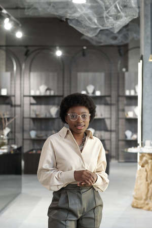 Happy young elegant shop assistant of jewelry boutique standing in front of camera on background of...