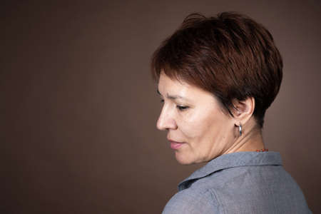 Close-up of mature woman with short brown hair posing at camera isolated on grey backgroundの写真素材