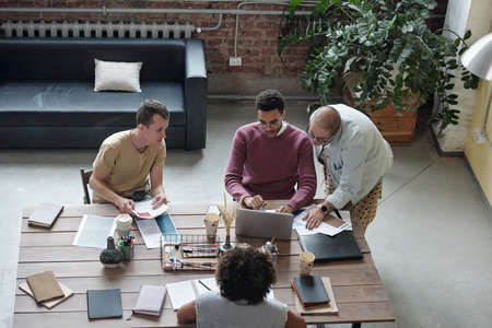 Young intercultural co-workers gathered in front of laptop discussing points of new business project...
