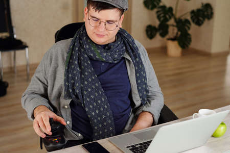 Man with disability rotating control panel of his wheelchair while sitting in front of laptop in...