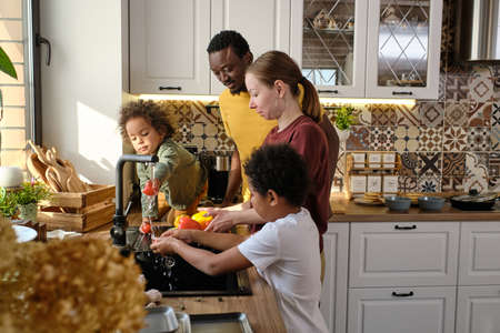 Young interracial family of father, mother and two sons washing fresh vegetables in the kitchenの写真素材