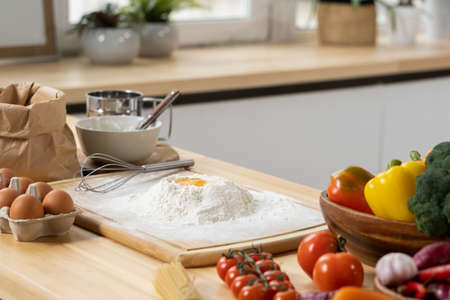 Pile of sifted flour with raw egg on top and other ingredients for homemade pastry on kitchen tableの写真素材