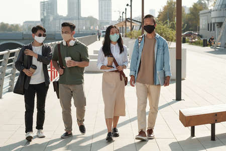 Young Asian colleagues in protective masks taking walk in park on sunny dayの写真素材