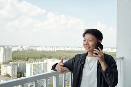 Happy young Asian businesswoman talking on mobile phone while standing on balconyの写真素材