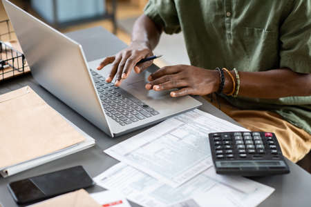 Hands of young African man typing on laptop keypad while working in the net and analyzing online...